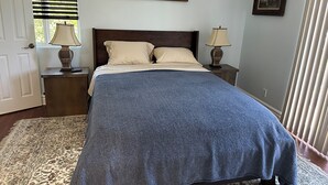 Quarto com uma cama grande, duas mesas de cabeceira com abajures, um quadro na parede e uma janela com persianas.
