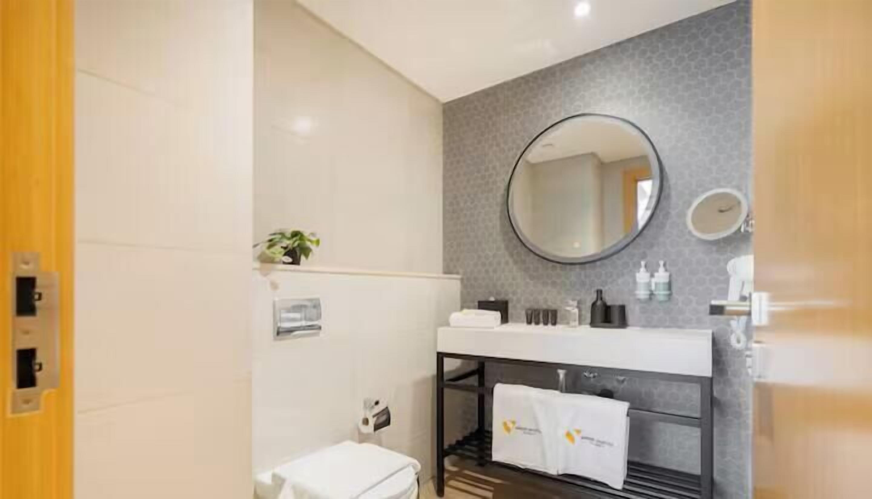 Une salle de bain moderne avec un lavabo blanc, un miroir rond et un porte-serviettes.