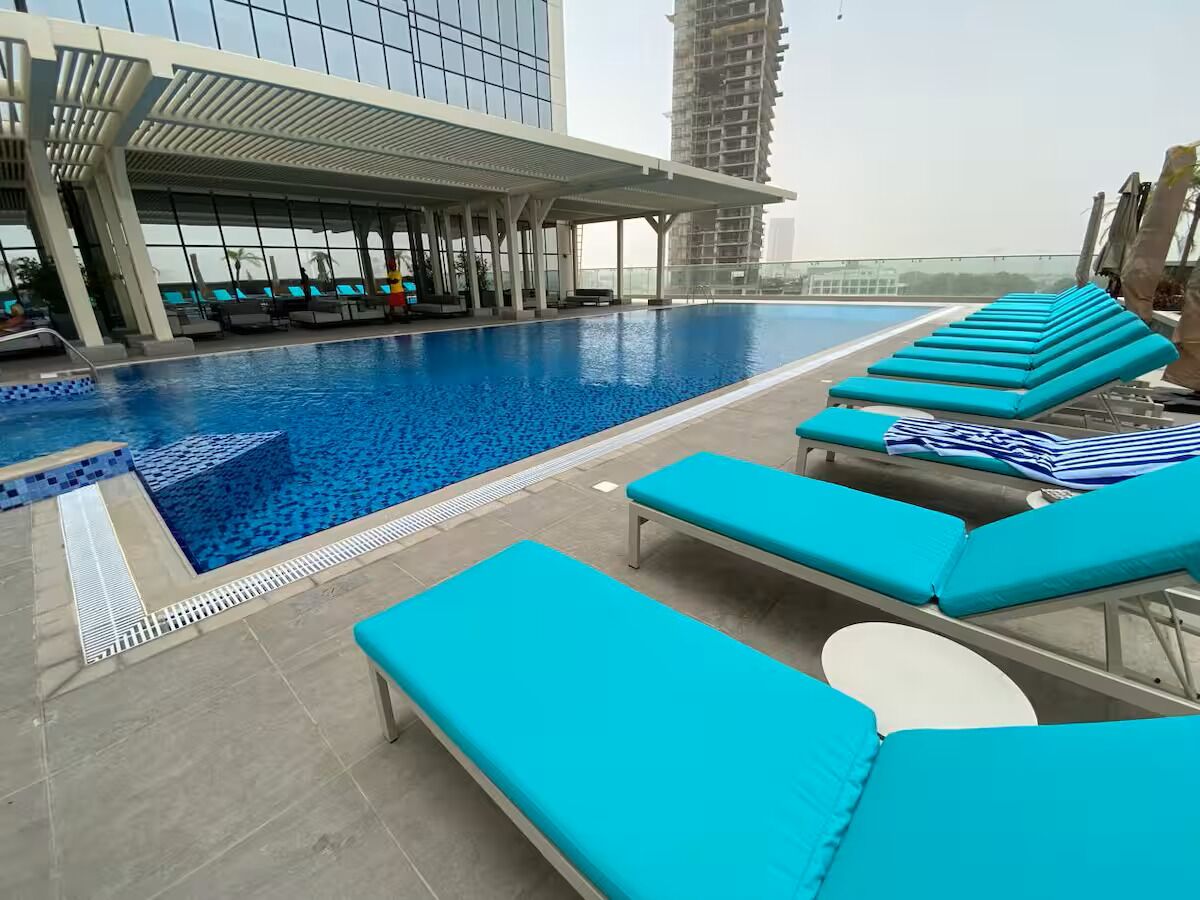 Piscina en la azotea con sillas reclinables azules y un área de estar techada.