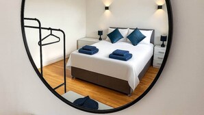 A modern bedroom with a bed, bedside tables, and a mirror. - Stoke Mandeville House | Sleeps up to 6-8 (Aylesbury)