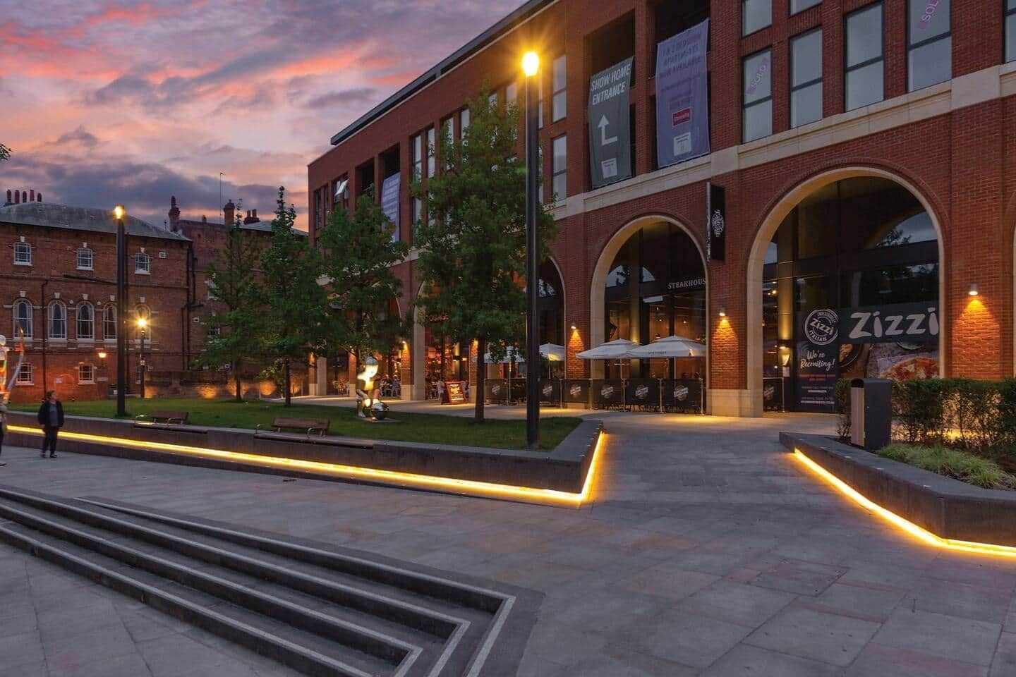 A modern building with a brick facade, large arched windows, and outdoor seating areas.