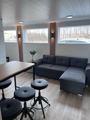 A modern interior with a grey sectional sofa, a wooden dining table, and black stools. - Kot apartment (Hvolsvöllur)