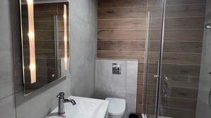 A modern bathroom with a white sink, a mirror, a toilet, and a glass-enclosed shower. - Kot apartment (Hvolsvöllur)