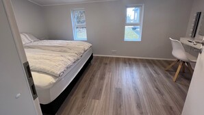 A bedroom with a bed, a desk, two windows, and a mirror. - Kot apartment (Hvolsvöllur)
