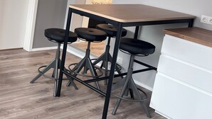 A modern kitchen with a wooden table and black bar stools, a white cabinet, and a mounted TV. - Kot apartment (Hvolsvöllur)