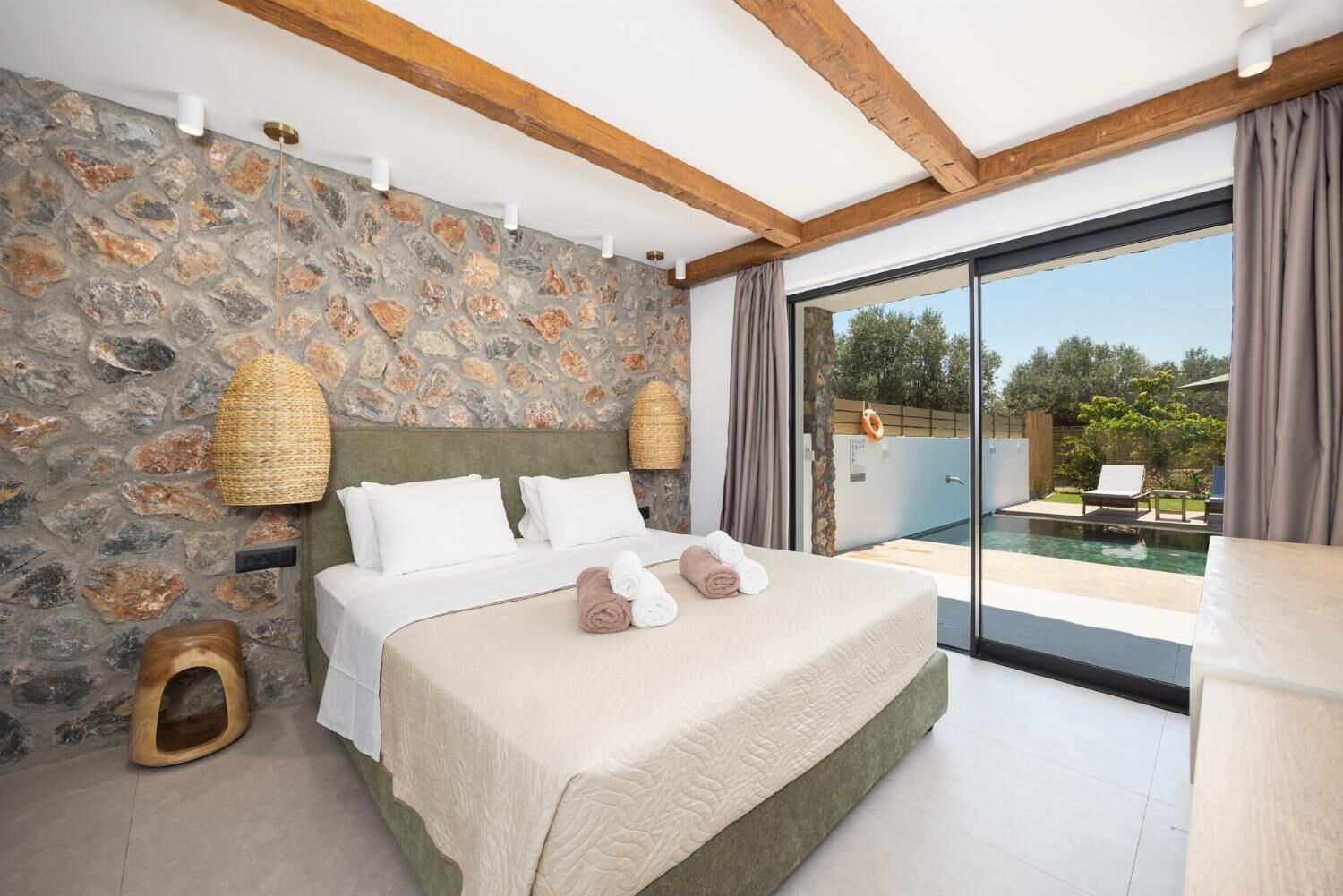 Ein Schlafzimmer mit Steinwand, einem Bett mit weißer Bettwäsche, einem Holz-Kopfteil und Blick auf einen Außenpool.