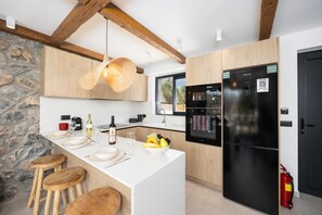 Eine moderne Küche mit Steinwand, Holzbalken, einer großen Kochinsel mit Sitzgelegenheiten und einem schwarzen Kühlschrank.