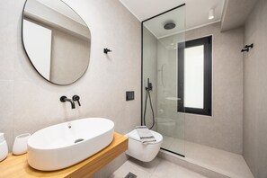Un bagno moderno con un lavabo ovale grande, una cabina doccia in vetro e uno specchio a parete.