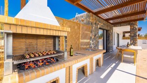 Cocina exterior con parrilla, pileta y comedor con mesa y sillas.