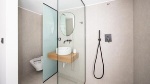 Un baño moderno con mampara de vidrio, lavamanos con espejo y ducha con cabezal de mano.