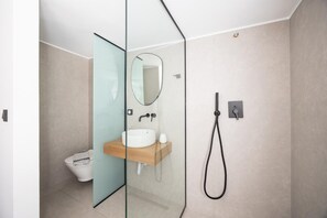 Ein modernes Badezimmer mit Glastrennwand, Waschbecken mit Spiegel und Dusche mit Handbrause.