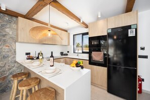 A modern kitchen with a large island, wooden accents, and a black refrigerator. - Villa Celestia - Two Bedroom Villa, Sleeps 4 (Afandou)