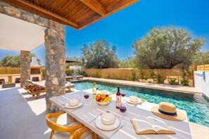 A poolside dining area with a table set for two, a bottle of wine, and a book. - Villa Celestia - Two Bedroom Villa, Sleeps 4 (Afandou)