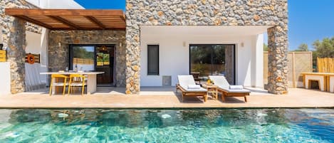 A modern villa with a stone facade, a pool, and outdoor seating.