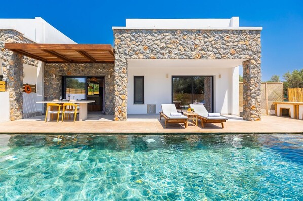 Eine moderne Villa mit Steinverkleidung, einem Pool und Außenmöbeln.