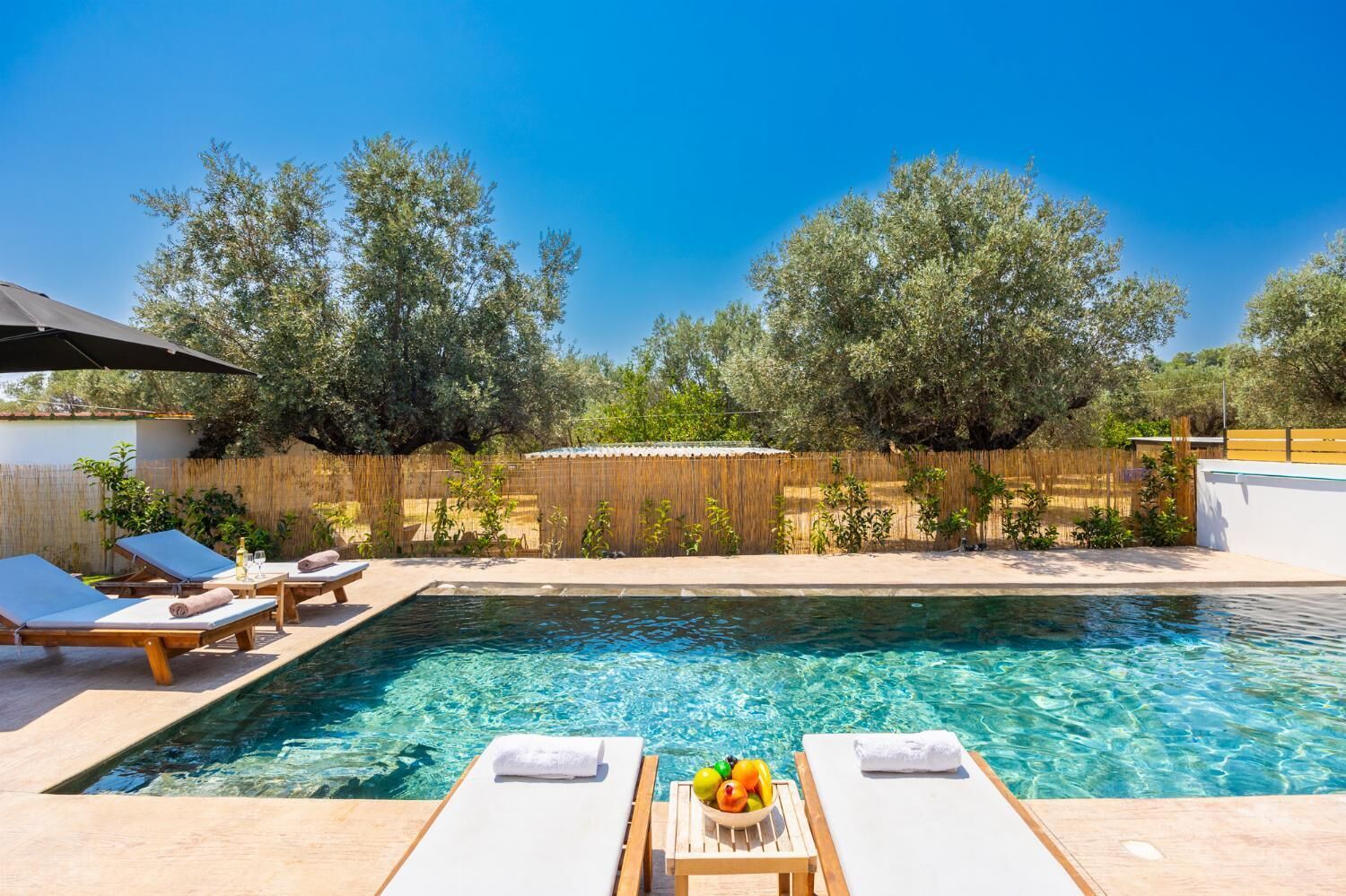A swimming pool with lounge chairs and a table with fruit.