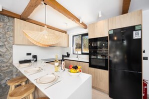 A modern kitchen with a black refrigerator, wooden cabinets, a stone wall, and a hanging light fixture. - Villa Amethysta - Two Bedroom Villa, Sleeps 4 (Afandou)