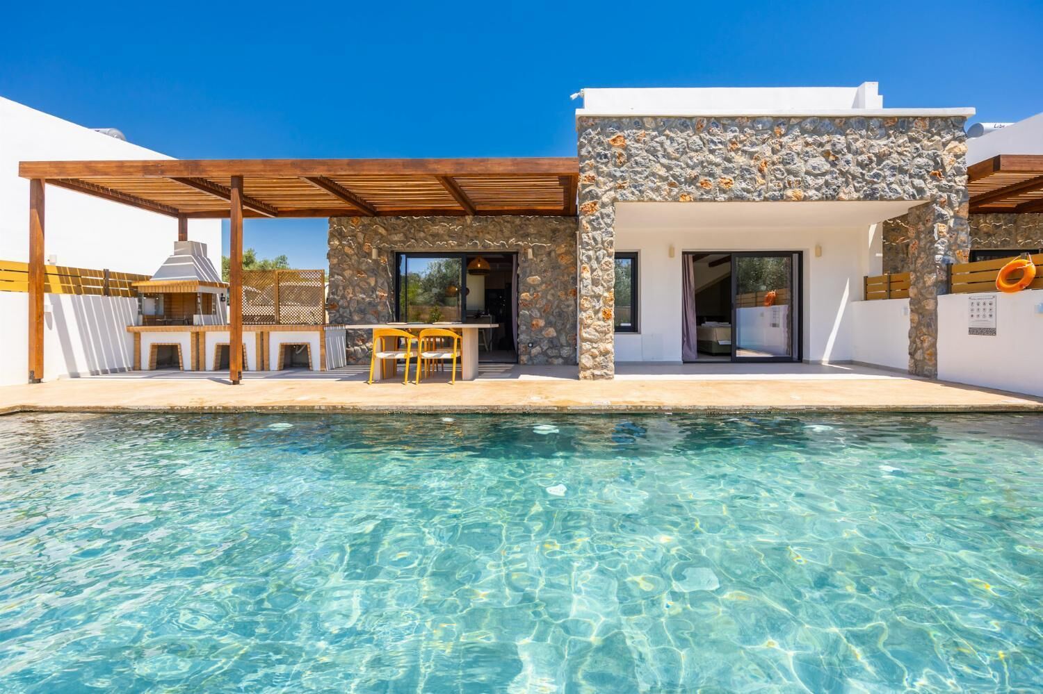 A modern house with a stone facade, a pool, and outdoor furniture.