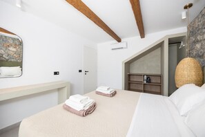 A bedroom with a bed, a bedside table, a mirror, a wardrobe, and a stone wall. - Villa Amethysta - Two Bedroom Villa, Sleeps 4 (Afandou)