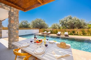A poolside dining area with a table set for two, a pool, and lounge chairs in the background. - Villa Amethysta - Two Bedroom Villa, Sleeps 4 (Afandou)