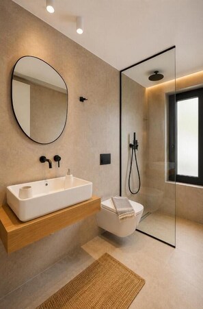 Ein modernes Badezimmer mit einem großen, ovalen Spiegel, einem rechteckigen Waschbecken, einer Duschkabine aus Glas und einem kleinen Handtuch auf dem Boden.