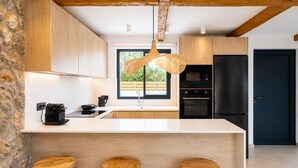 Une cuisine moderne dotée d’un grand îlot central, de tabourets en bois, d’un luminaire suspendu et offrant une vue sur la verdure environnante.