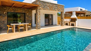 Une maison moderne avec une façade en pierre, une piscine et un espace salon extérieur.