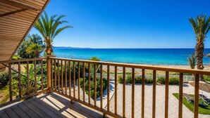Eine Holzterrasse mit Geländer, die auf einen Strand mit Palmen und wolkenlosem, blauem Himmel blickt.