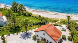 Ein Küstengrundstück mit einem Haus mit rotem Dach, einem Sandstrand und einem Segelboot in der Ferne.