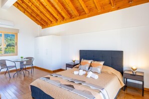 A bedroom with a wooden ceiling, a bed with pillows, a bedside table, a chair, and a window with a view. - Villa Kochili - Two Bedroom Villa, Sleeps 4 (Nea Dimmata)