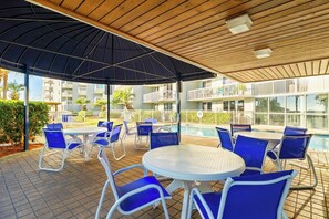 An outdoor pool area with blue chairs and tables, surrounded by a wooden pergola and a white fence. - Pelican Beach Resort · Ocean Views | 3 Pools, Hot Tub, Courts, Gym & Balcony (Destin)