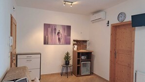 A compact living space with a kitchenette, a wooden door, a clock, and a painting on the wall. - Pansion Dovodja - Close to the beach and the center - your vacation home / Apartment 9 (Vodice)