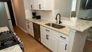 A kitchen with white cabinets, a granite countertop, a stainless steel sink, a coffee maker, and a stove.