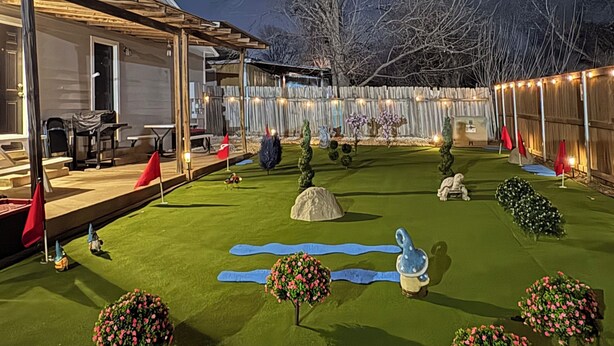 A well-maintained backyard with artificial grass, a variety of decorative plants, and a wooden deck.