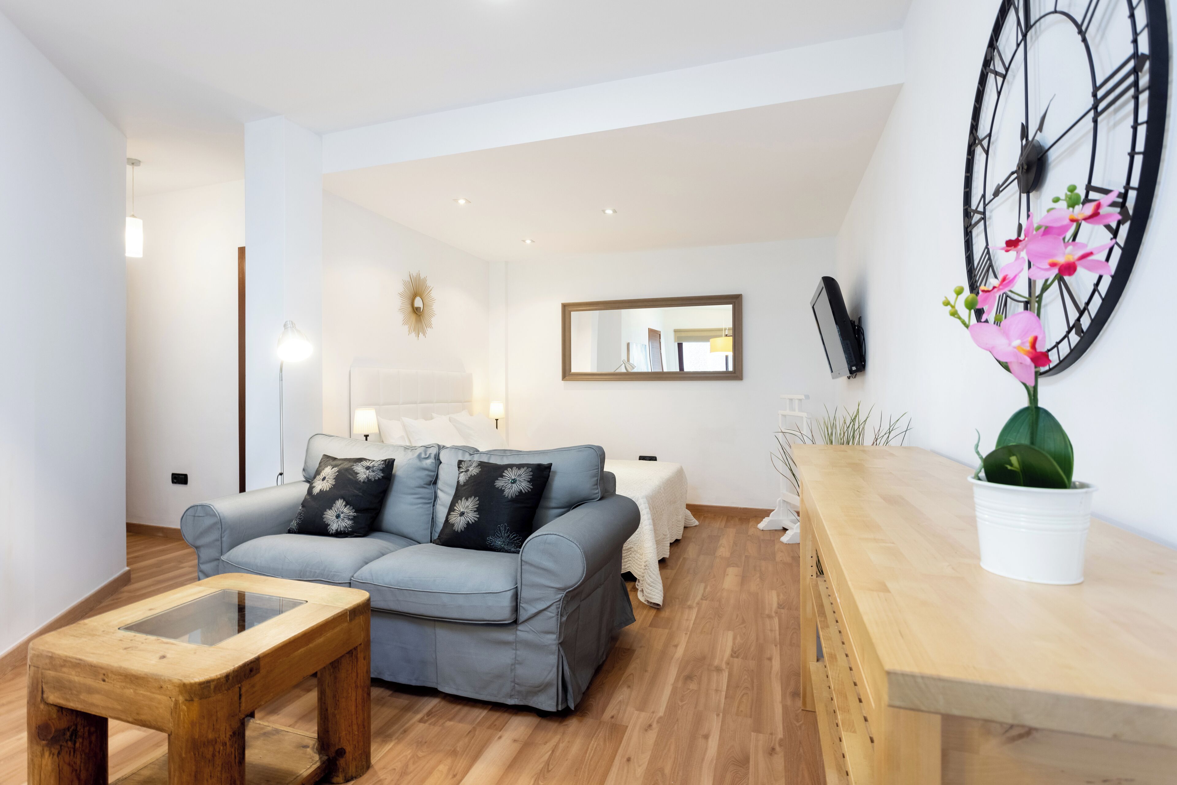 A modern living room with a grey sofa, a wooden coffee table, and a large wall clock.