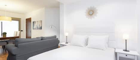 Una habitación de hotel moderna con una cama grande, un sofá gris, un escritorio y una lámpara.
