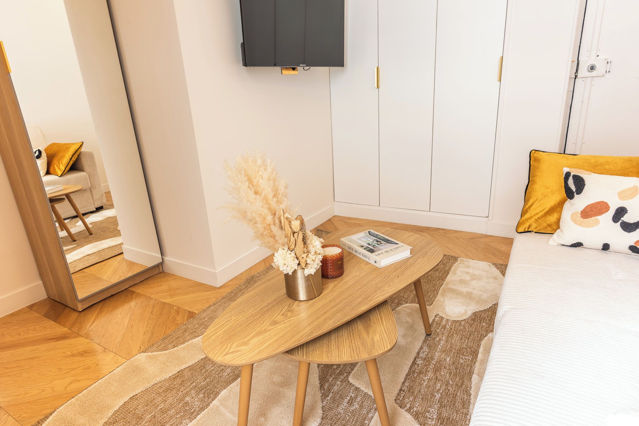 Une chambre à coucher avec un lit, une table de chevet en bois, un miroir, une télévision et une porte.