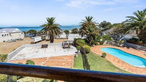 A residential area with a swimming pool, parked vehicles, and a view of the ocean.