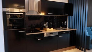 A modern kitchen with black cabinets, stainless steel appliances, and a wooden countertop. - Apartments Kellergasse - Blue Apartment (Purbach am Neusiedlersee)