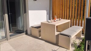 Um pátio com mesa, banco, porta de vidro e cerca de madeira.