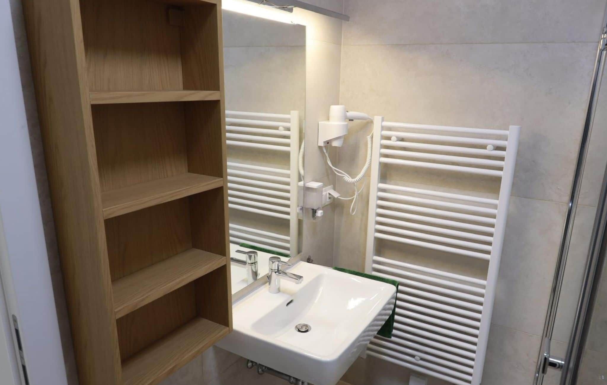 A modern bathroom with a white sink, wooden shelves, a mirror, and a towel rack.