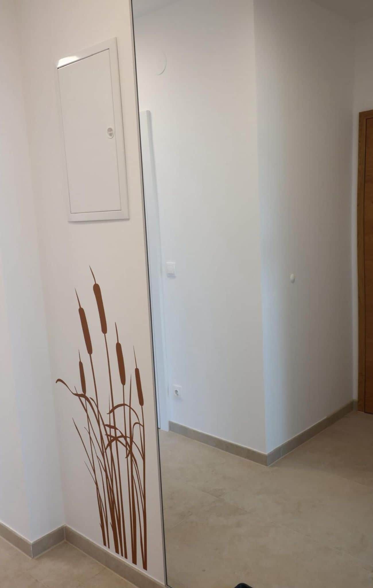 Un couloir avec une porte blanche, un interrupteur et un mur orné d’un motif végétal décoratif.