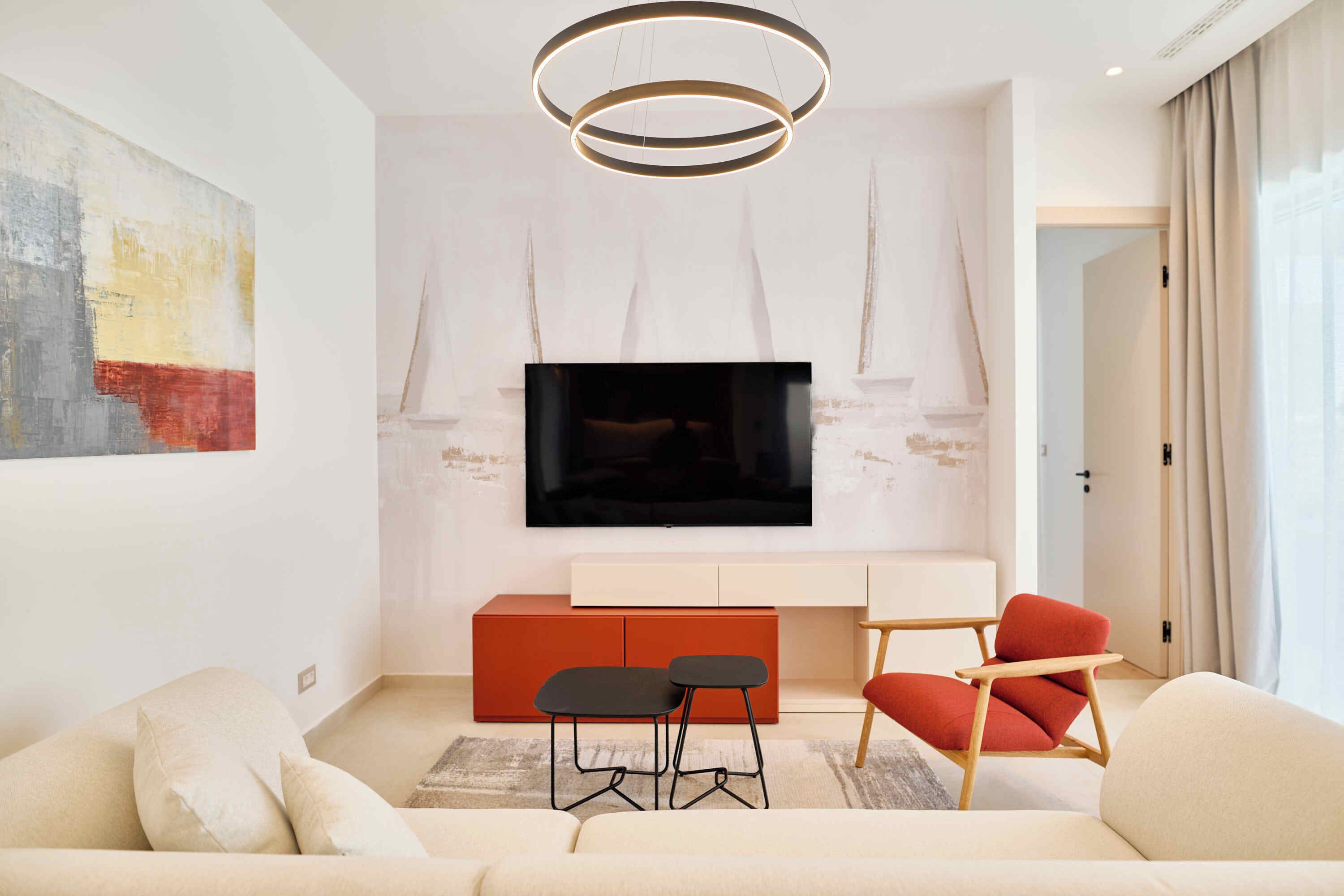 Una sala moderna con un televisor de pantalla plana montado en una pared blanca, un mueble rojo, un sofá beige y una silla roja.