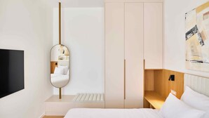 Una camera d'hotel moderna con un letto, una TV, uno specchio e una testiera in legno.