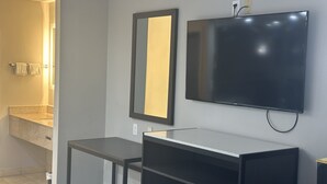 A modern bathroom with a large mirror, a flat-screen TV mounted on the wall, and a small table. - Red Roof Inn Media, PA (Media)