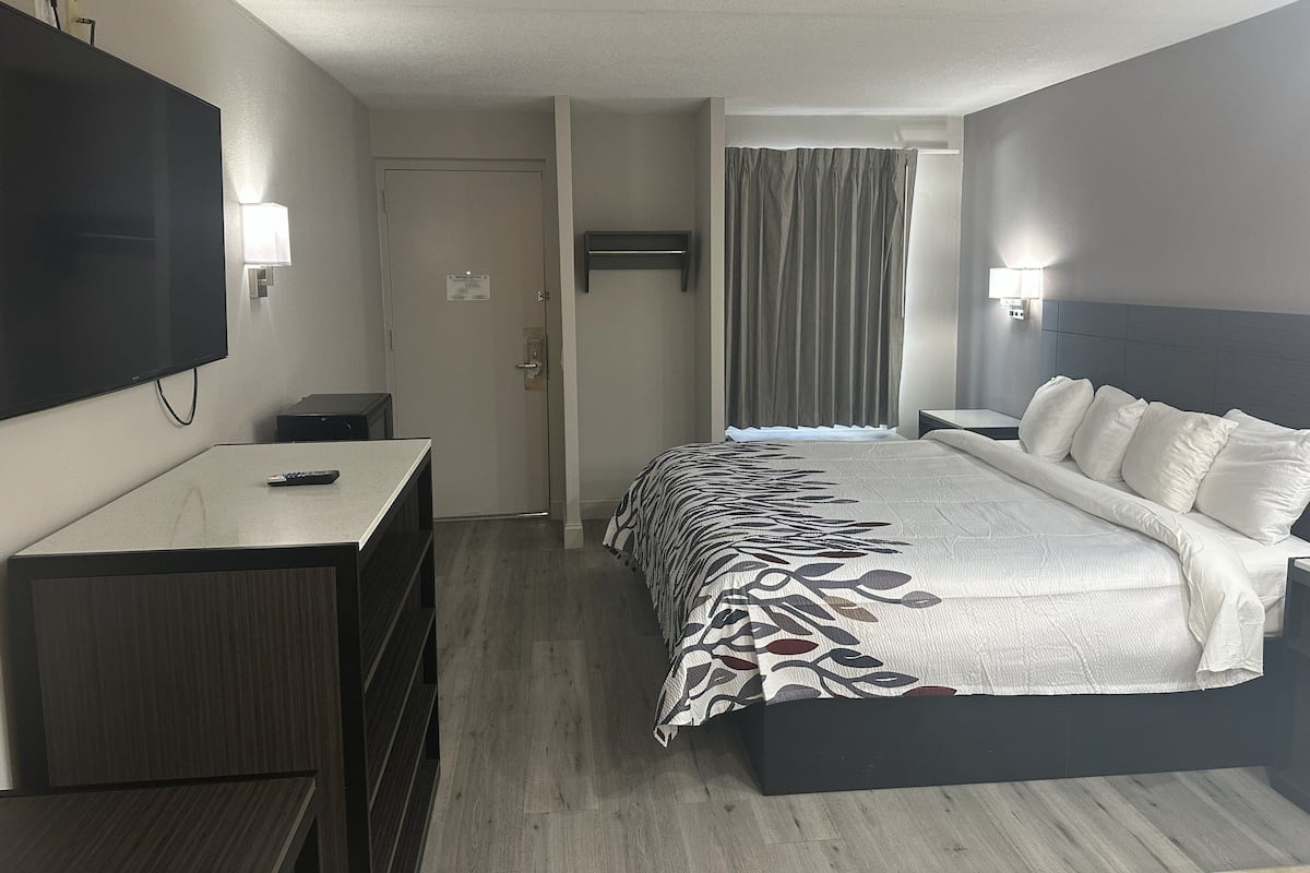 A hotel room with a bed, a desk, a TV, and a door.