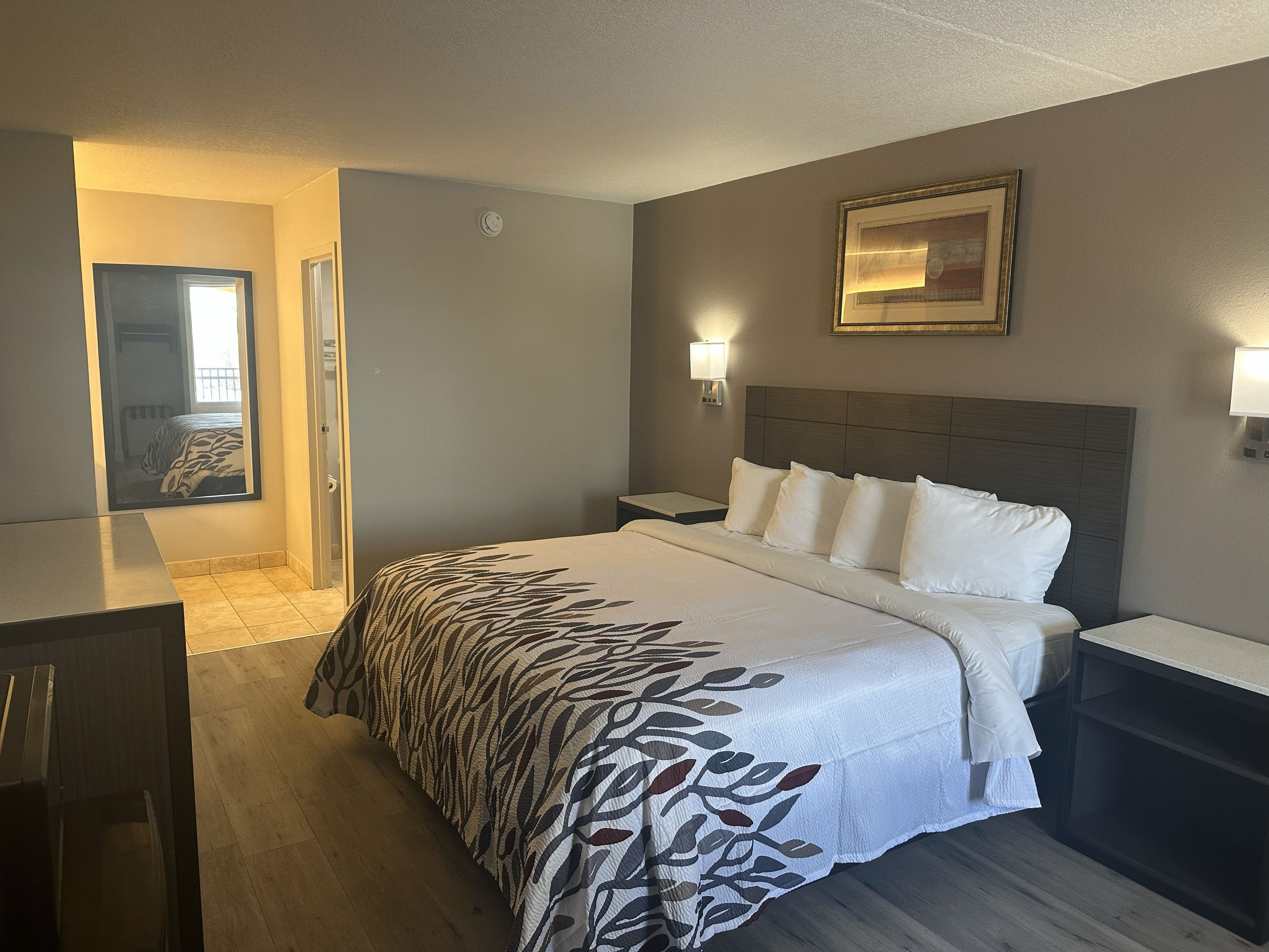 A hotel room with a bed, bedside tables, a desk, and a framed picture on the wall.
