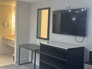 Un baño moderno con un espejo grande, un televisor de pantalla plana en la pared y una mesita.