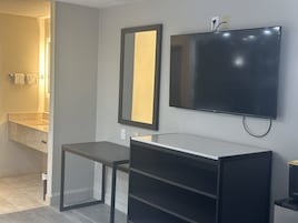Un baño moderno con un espejo grande, un televisor de pantalla plana en la pared y una mesita.