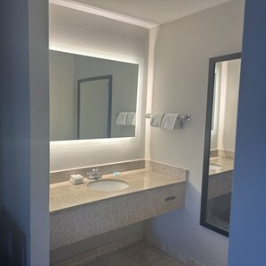 A bathroom with a granite countertop, a sink, a mirror, and a towel rack. - Red Roof Inn Media, PA (Media)